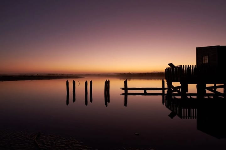 Photo of dawn across a still lake in the South Island, New Zealand, with a jetty and pilons