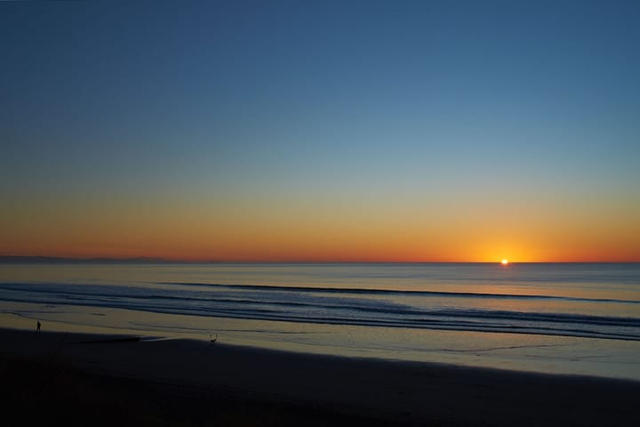 Photo of the sun setting over calm seas from the shore, South Island, New Zealand